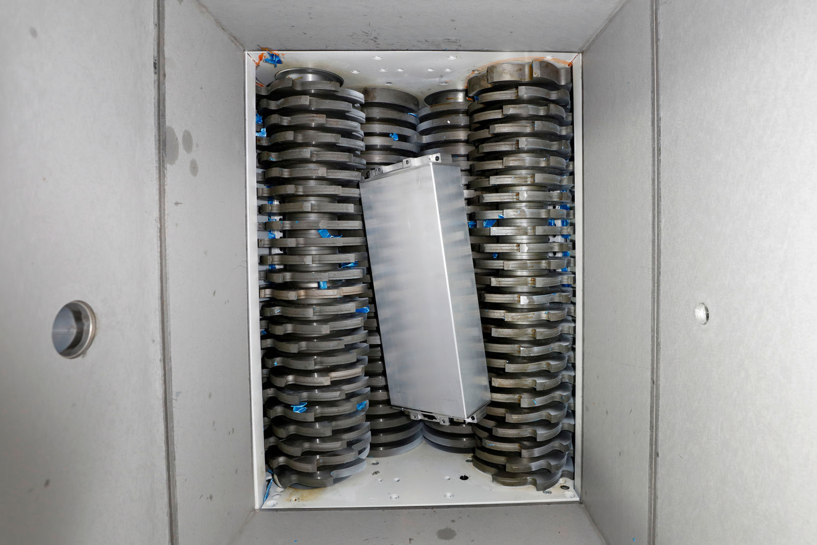 Eine leistungsstarke industrielle Schreddermaschine mit gegenläufigen rotierenden Klingen, die eine rechteckige Batterie zerkleinert. Die Maschine ist in einem geschlossenen Metallgehäuse untergebracht.