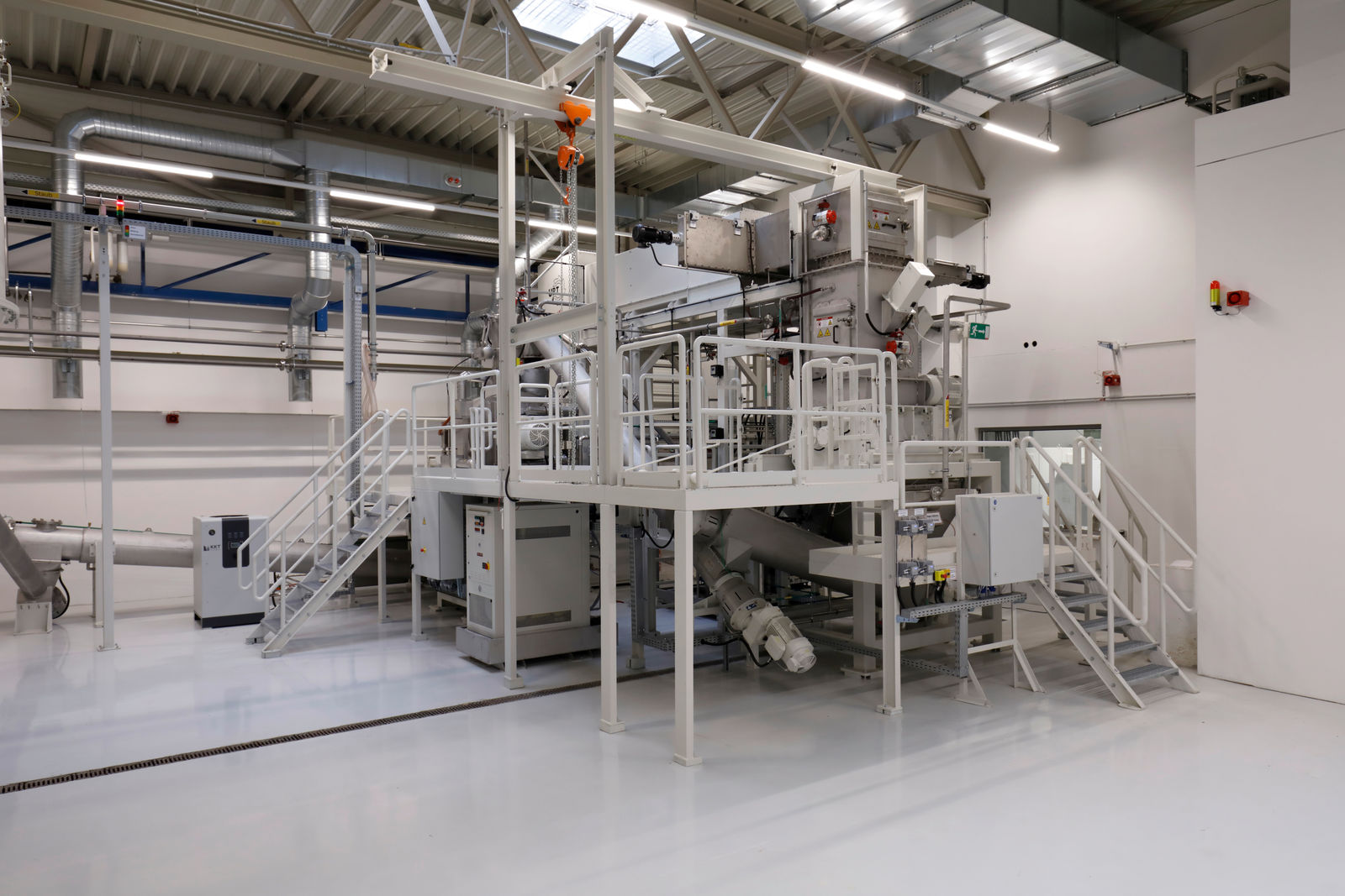 Modern battery recycling facility with conveyor belts and piping systems in a clean industrial hall.