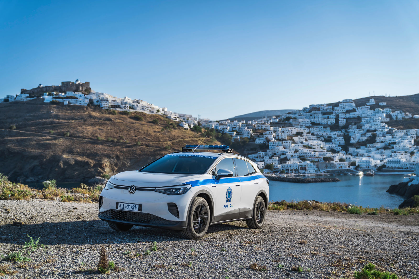 A Volkswagen police vehicle of the Greek police is parked on a hill overlooking a coastal town with white houses.