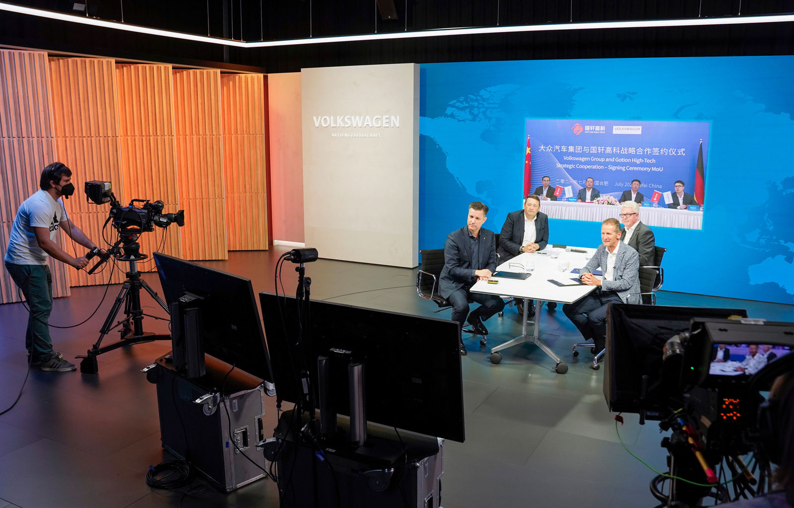 Ein professionelles TV-Studio mit einem runden Tisch, an dem vier Männer eine Vertragsunterzeichnung durchführen. Im Hintergrund ist eine große digitale Leinwand mit chinesischen und deutschen Flaggen sowie dem Schriftzug „Volkswagen Group und Gotion High-Tech – Strategic Cooperation Signing Ceremony MoU“ zu sehen. Kameraleute und Produktionsmonitore befinden sich im Vordergrund.