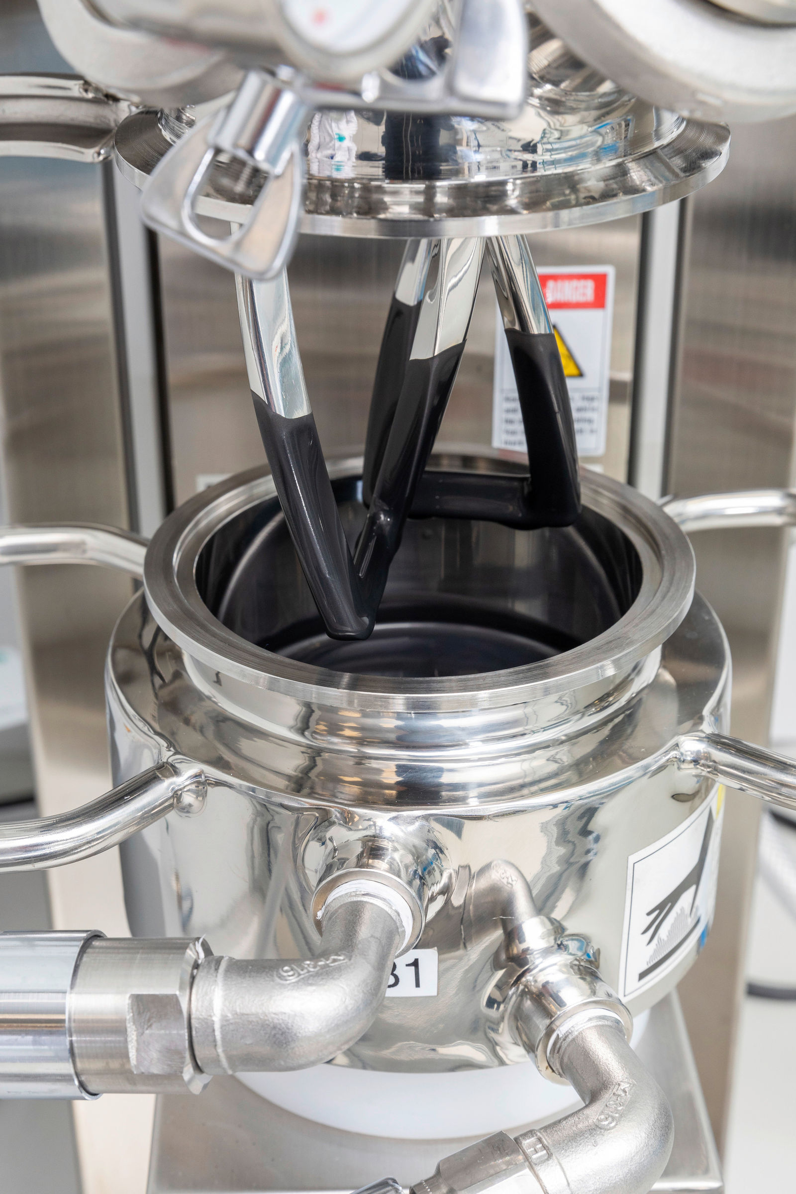 A close-up of machine components in a lab, with black material being transferred into a metal container.