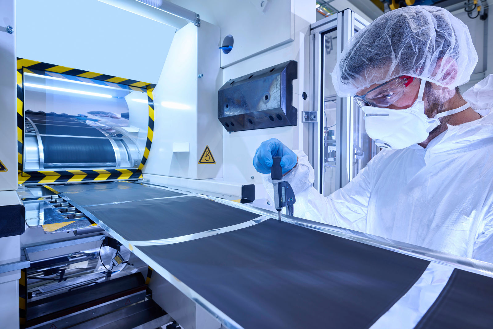 A worker is wearing a protective suit and using a measuring instrument to inspect a production process in a factory.