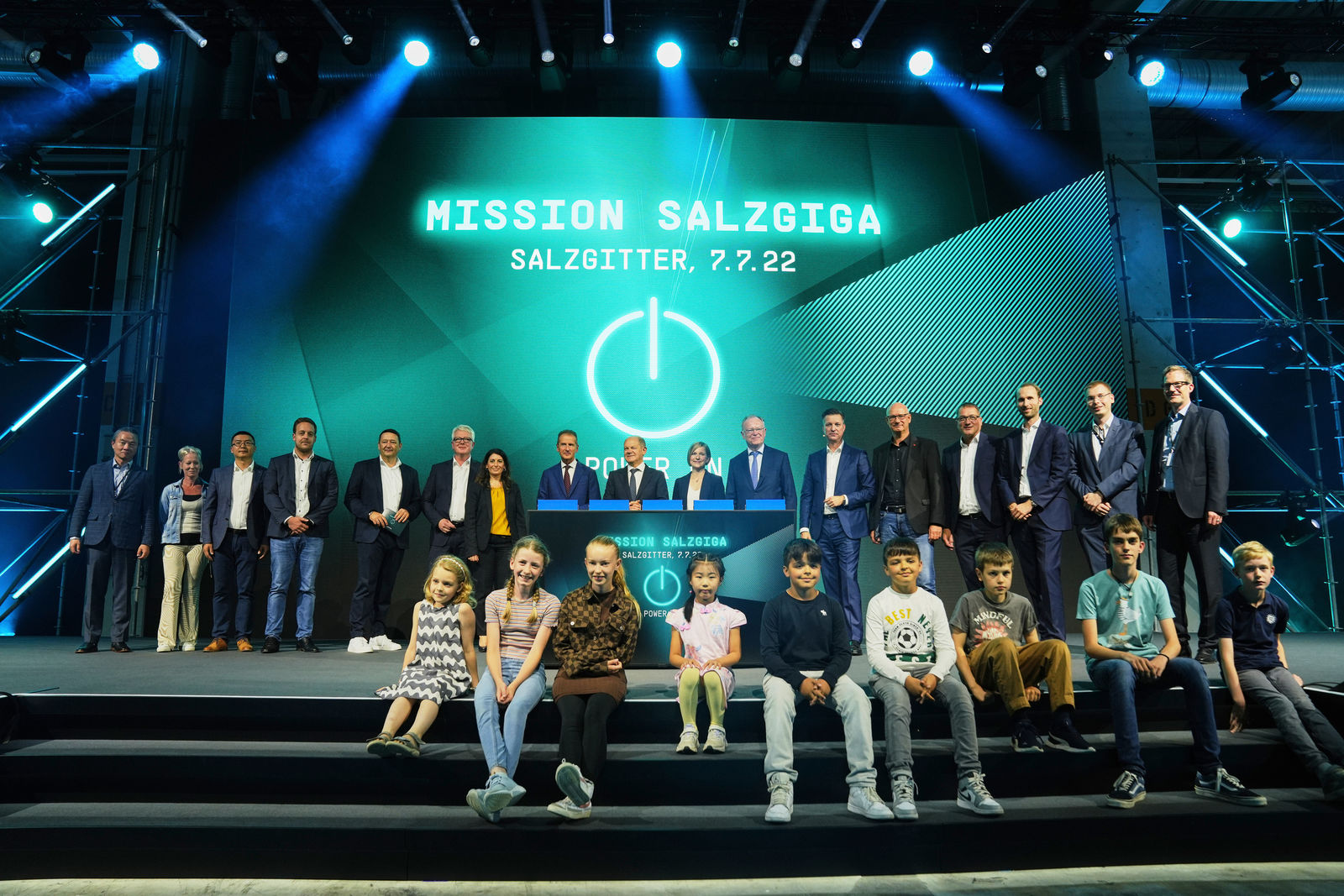 Group photo from the "Mission Salzgiga" event on July 7, 2022, in Salzgitter. Several Volkswagen executives stand on stage, flanked by children, with the event logo displayed on a large screen in the background.