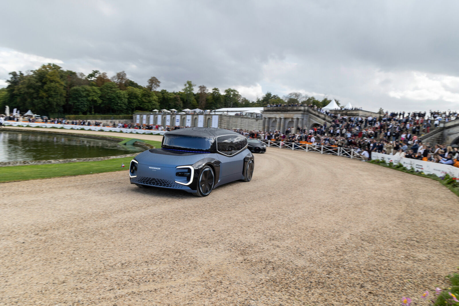 A futuristic concept car from Volkswagen drives on a gravel road in front of an audience.