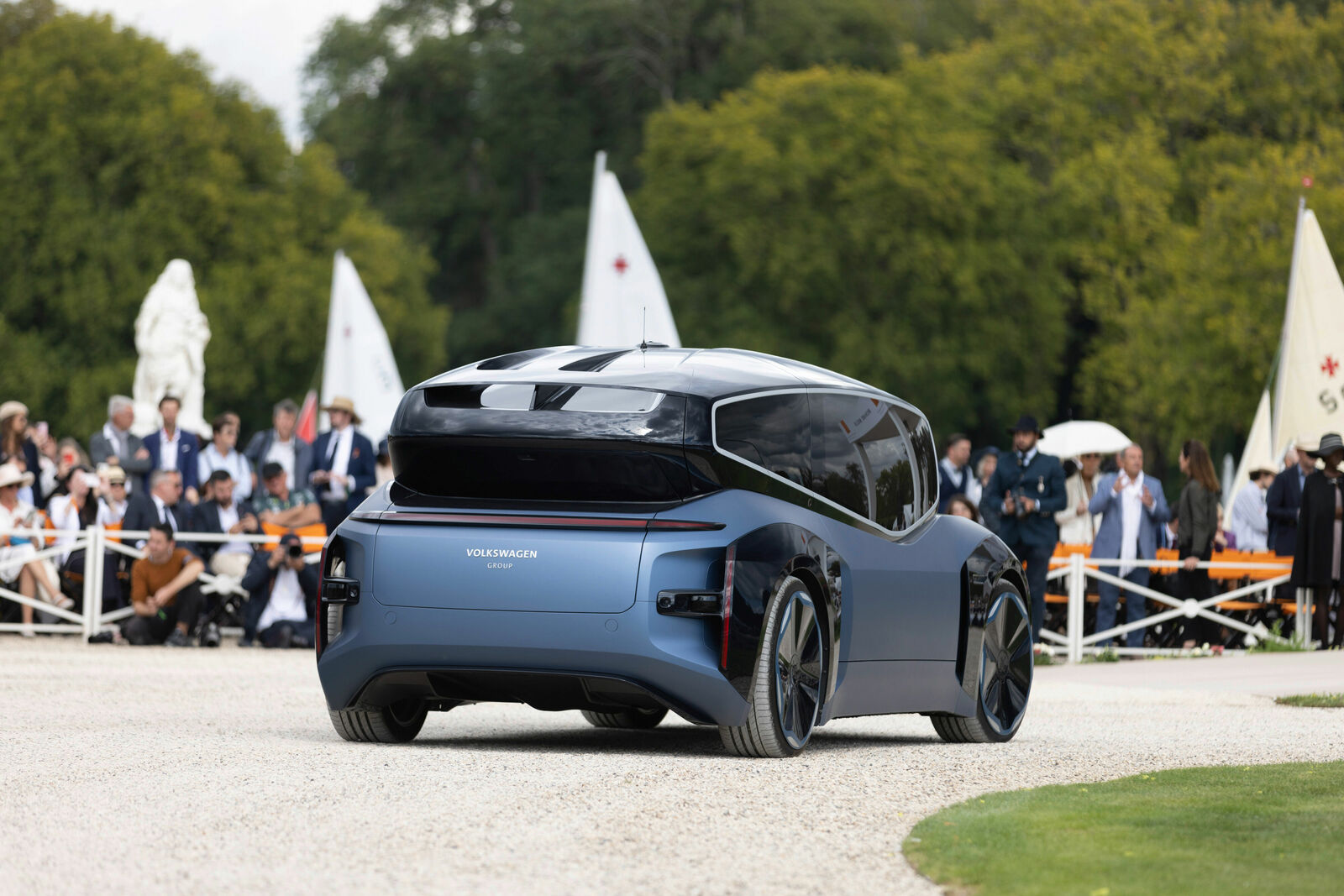 A futuristic Volkswagen concept car drives through an elegant event with spectators in the background.