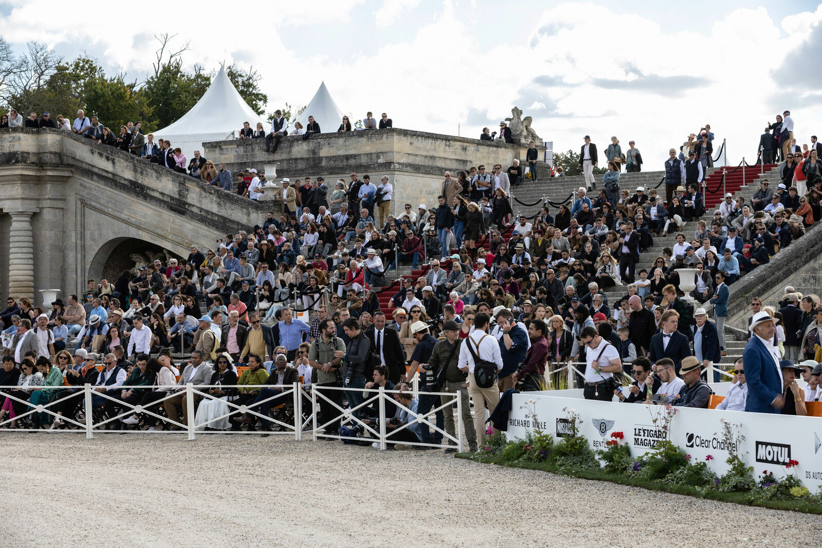 A large crowd gathers on a historic stone staircase and surrounding areas during an exclusive outdoor event.