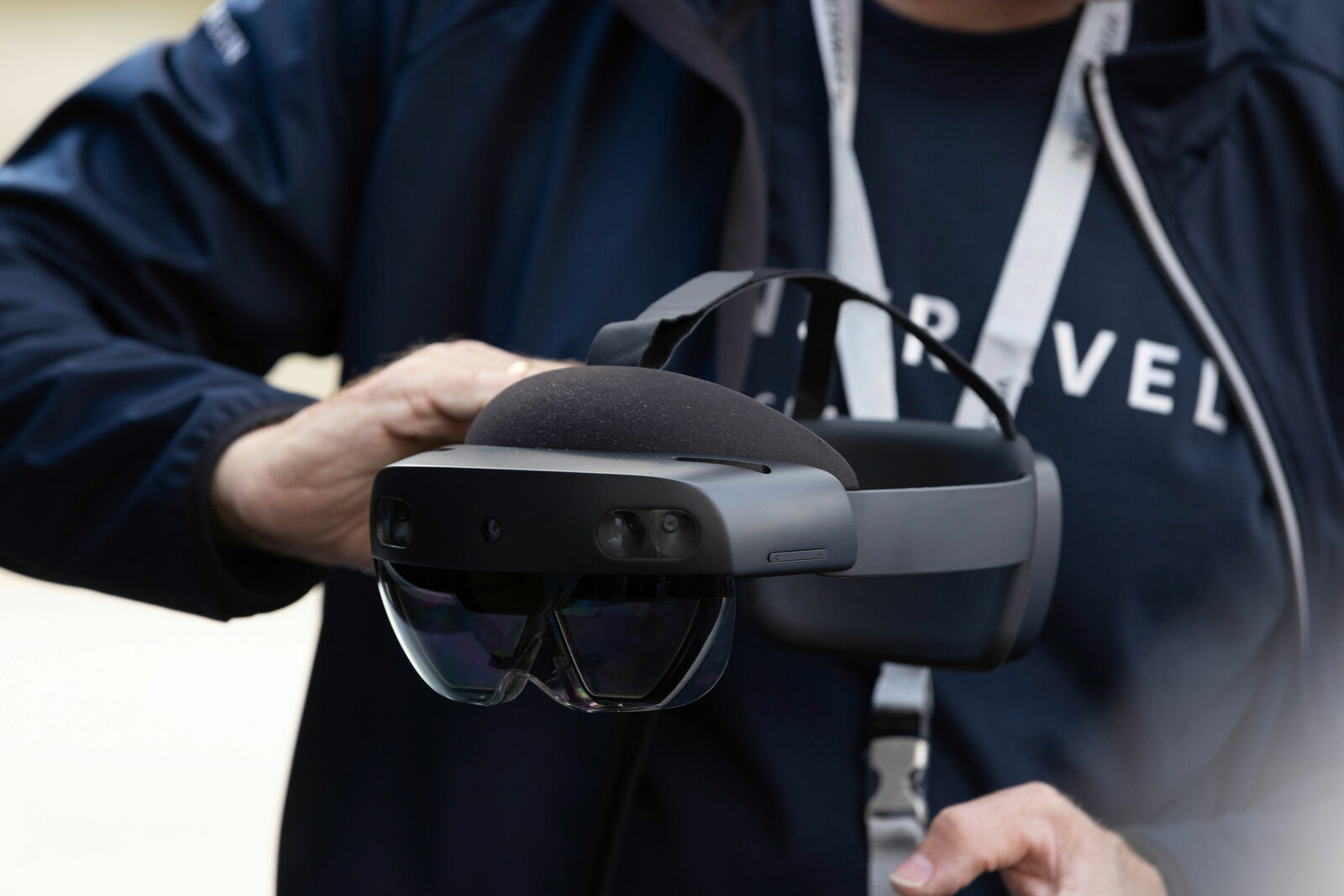 A person wearing dark clothing holds a modern mixed-reality headset with a transparent visor and multiple camera sensors at the front.