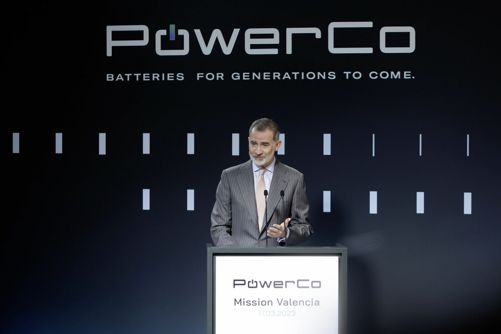 Ein Mann in Anzug spricht bei einer Veranstaltung von PowerCo vor einem dunklen Hintergrund mit dem Slogan „Batteries for generations to come.“