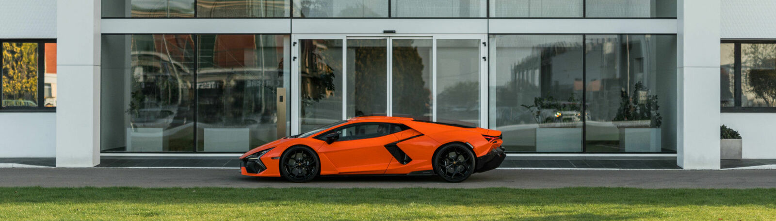 Orange Lamborghini Revuelto stands in front of a modern house.