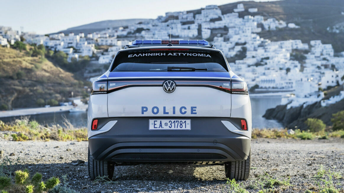 A Volkswagen police car is parked in a mountainous area with a Greek town in the background.