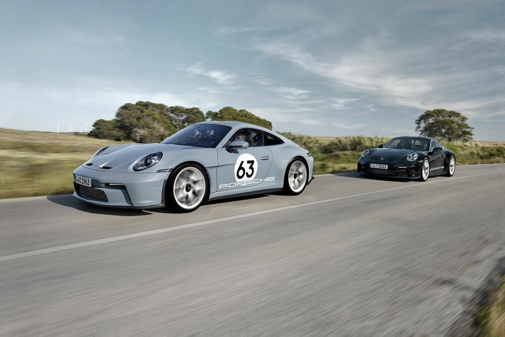 Two Porsche 911 models driving on a country road