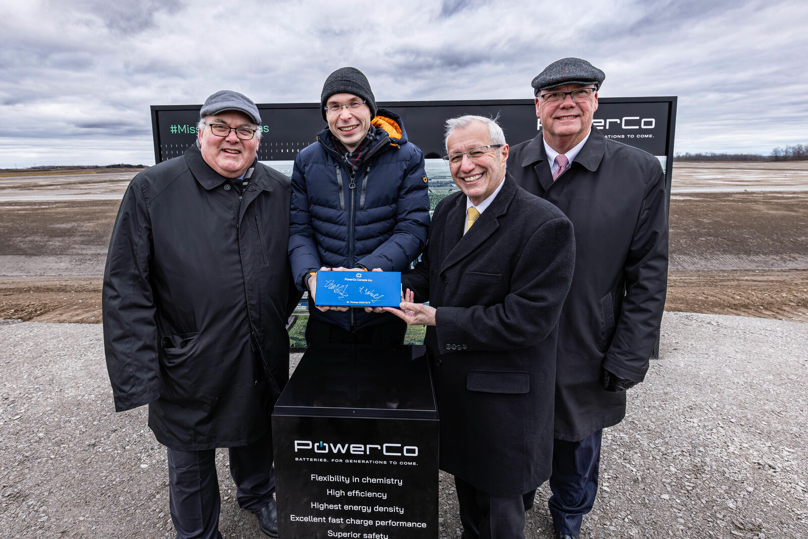 Four people with signed PowerCo battery in front of the construction site