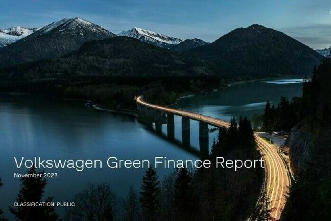 Nächtliche Szene mit einem beleuchteten Brückenverkehrsweg, der sich über einen ruhigen Fluss zwischen bewaldeten Bergen erstreckt. Im Vordergrund steht 'Volkswagen Green Finance Report November 2023'
