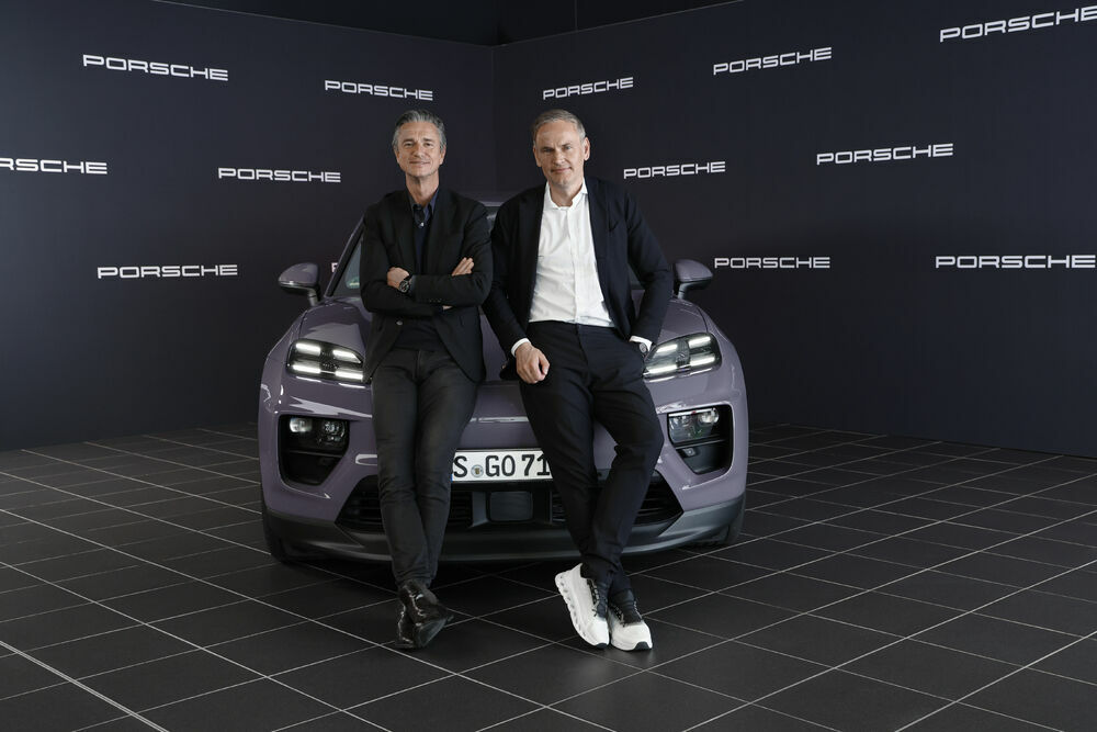 Zwei Männer in Business-Kleidung lehnen an einem lila Porsche vor einem dunkelblauen Hintergrund mit wiederholtem Porsche-Logo