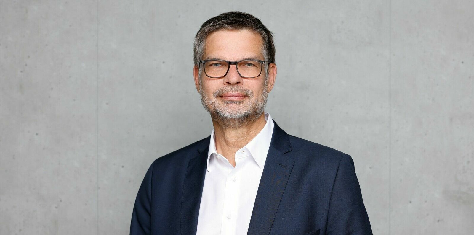 Portrait of Dirk Voeste in business attire against a grey background.