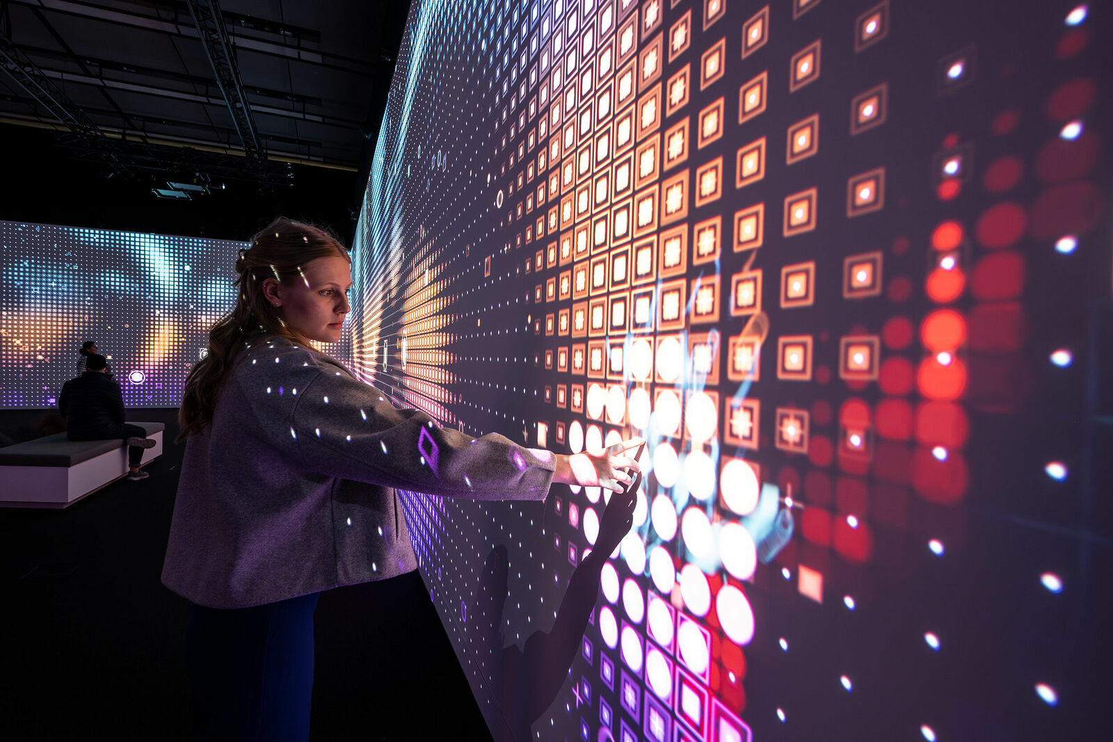 A person interacts with a wall display showing a colorful pattern of illuminated squares.