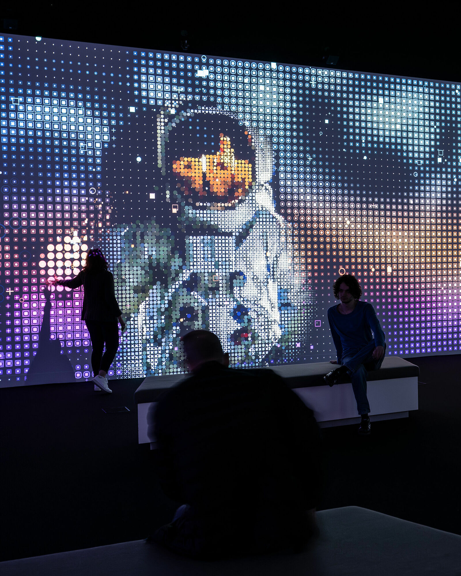 Besucher betrachten ein großes Wanddisplay mit pixeligen Darstellungen eines Astronauten im Weltall.