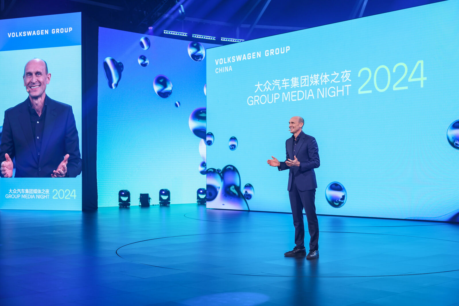 Ein Redner steht auf der Bühne während der Veranstaltung "Group Media Night 2024", und große Bildschirme zeigen den Titel und das Branding der Veranstaltung in Englisch und Chinesisch.