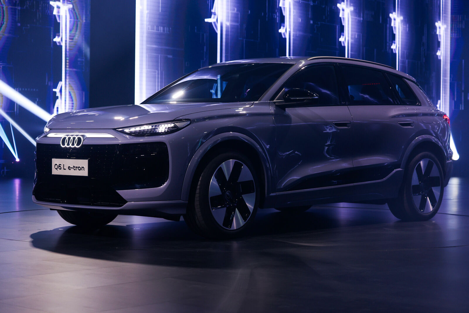 Ein metallic-grauer Audi Q6 e-tron SUV wird in einem schwach beleuchteten Ausstellungsraum mit futuristischer Beleuchtung im Hintergrund präsentiert.
