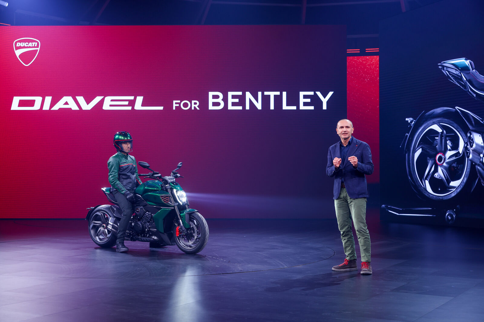 Ein Bild von einer Präsentation auf einer Automesse, auf der ein grünes Ducati-Motorrad neben einem Sprecher präsentiert wird.