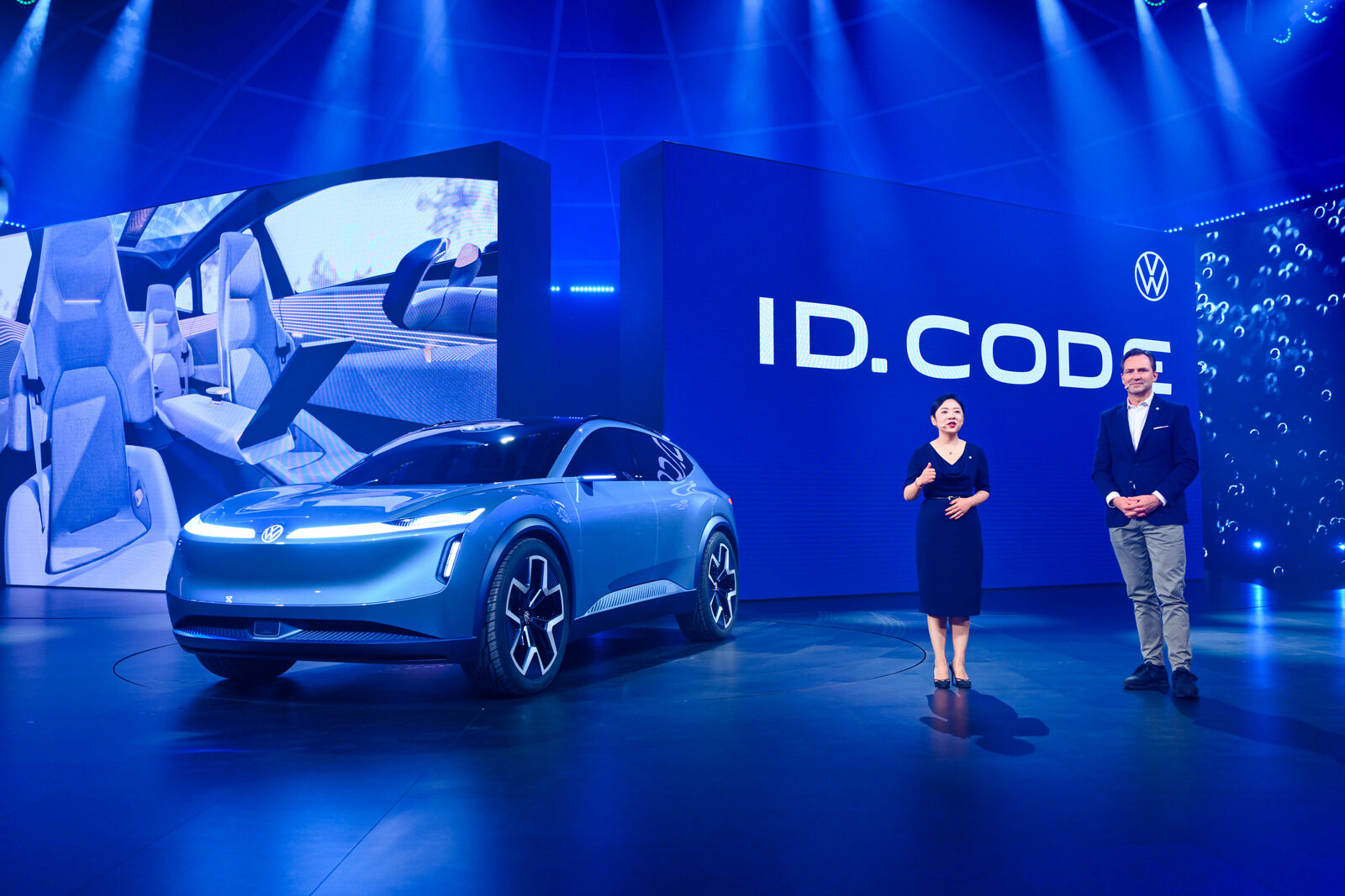 Ein metallisch-blauer Volkswagen ID. Code SUV-Konzept wird unter heller blauer Beleuchtung in einem futuristischen Ausstellungsraum gezeigt.