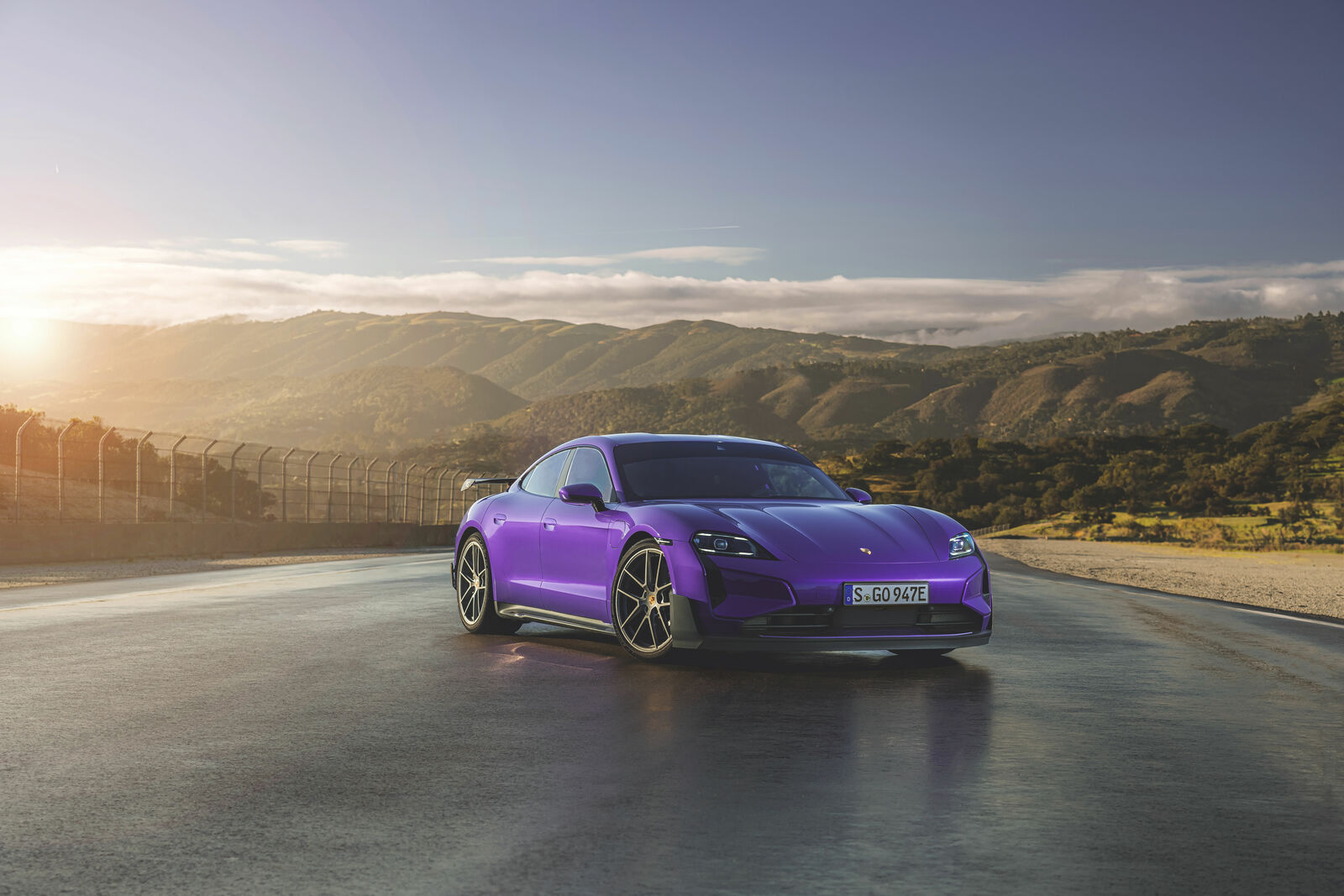 An image of a bright violet sports car parked on a racetrack, overlooking sunlit mountains in the background.
