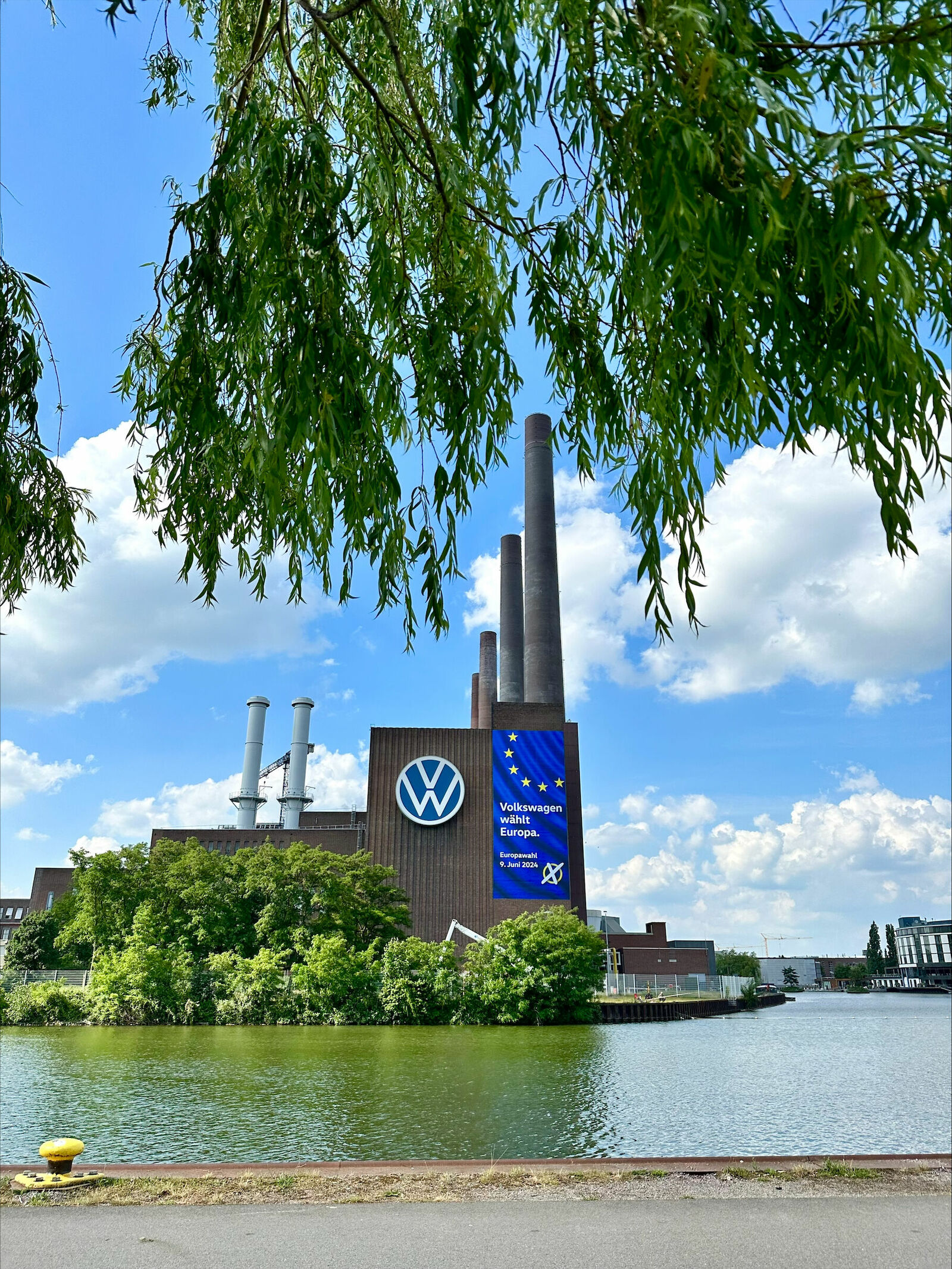 Ein großes Volkswagen-Werksgebäude mit einem Banner, das für die Europawahl am 9. Juni 2024 wirbt, mit einem blauen Hintergrund und gelben Sternen der EU-Flagge.