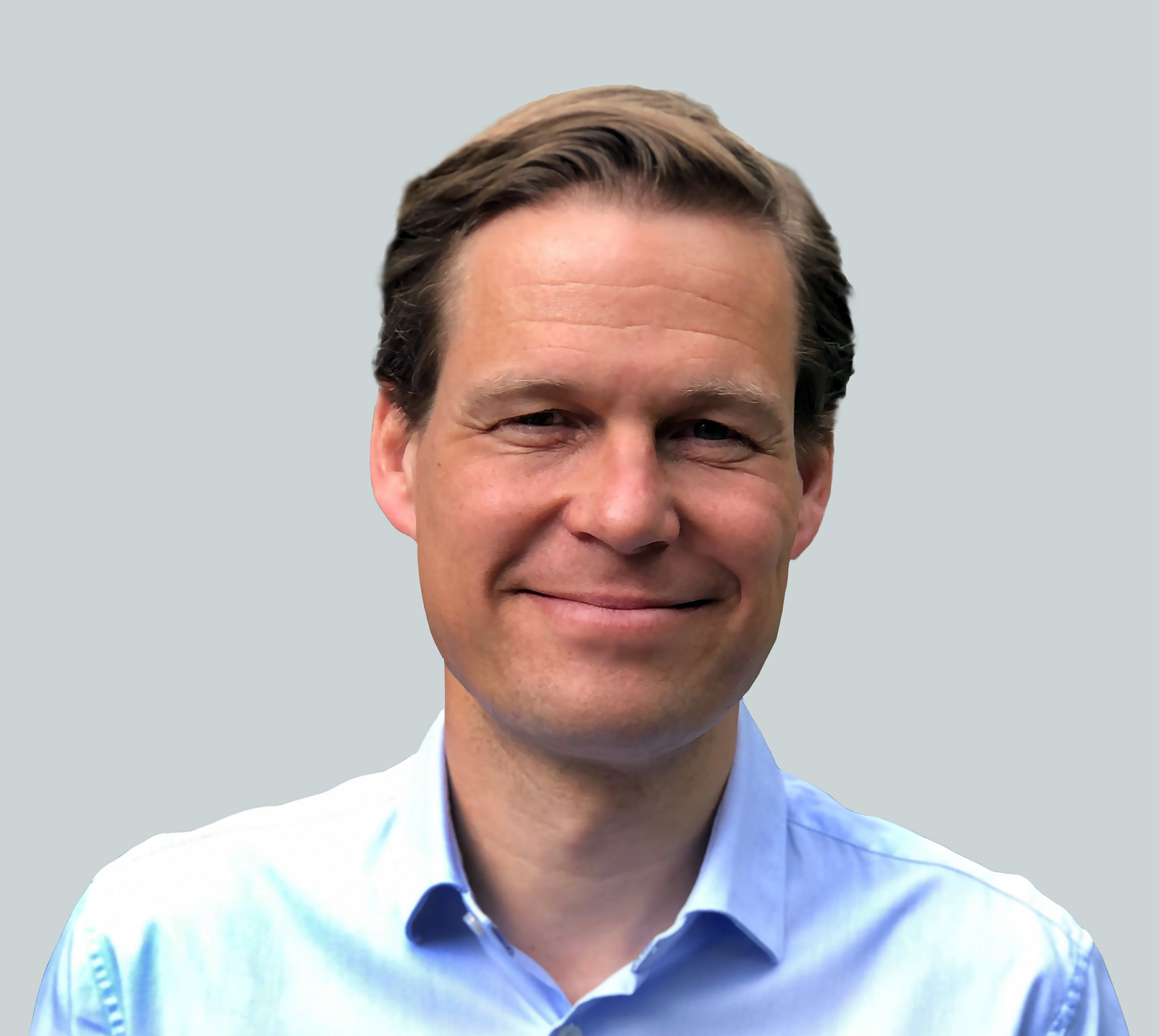 Porträt eines lächelnden Mannes mit braunem Haar, der ein hellblaues Hemd trägt und vor einem neutralen Hintergrund steht.