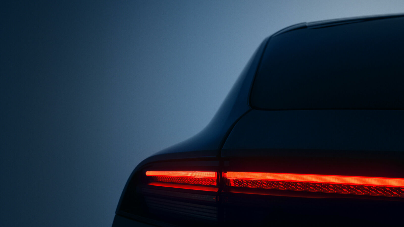 Rear view of a car in low light with a glowing red taillight.
