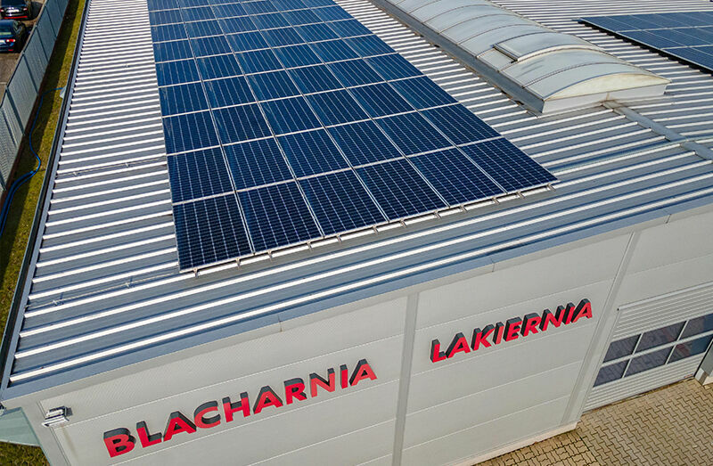 An industrial building with the words "Blacharnia Lakiernia" on the facade. Solar panels are installed on the roof.