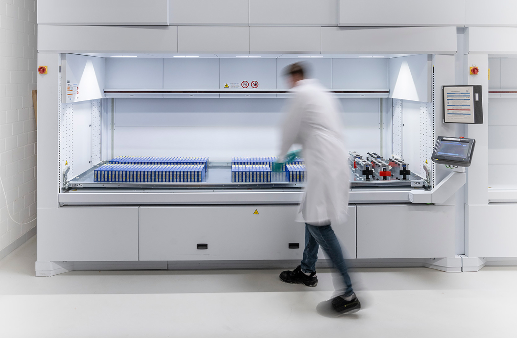 Laborant in weißem Kittel arbeitet an einem automatisierten Lager- und Verarbeitungssystem mit vielen Probenröhrchen.