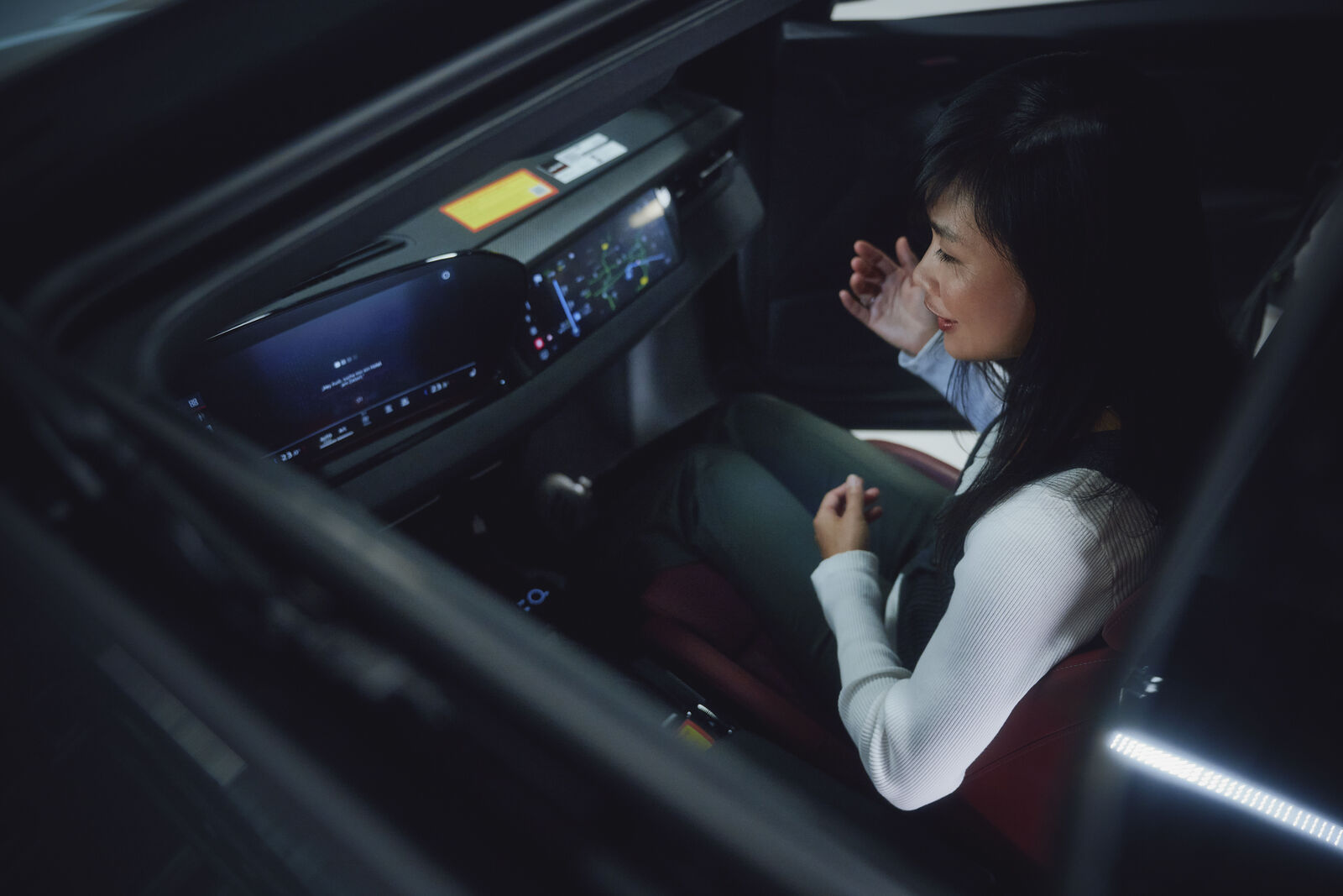 Frau sitzt im Innenraum eines modernen Autos und interagiert mit dem digitalen Cockpit-Display.