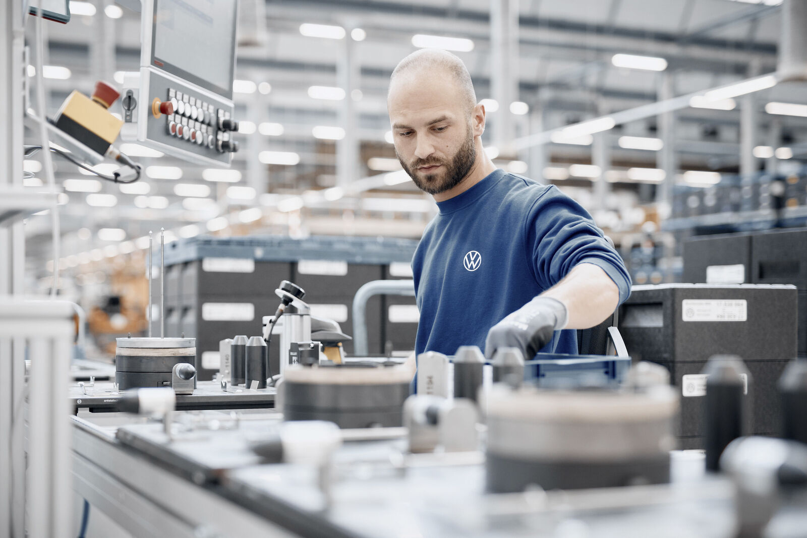 Mitarbeiter in VW-Arbeitskleidung arbeitet an einer Fertigungsstation in einer Produktionshalle.