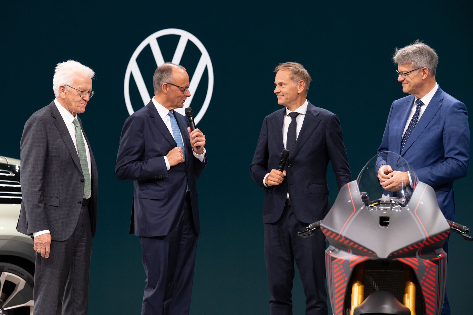 Oliver Blume (second from right) shows Chancellor Friedrich Merz (second from left), Baden-Württemberg's Minister President Winfried Kretschmann (left), and Minister of Transport Patrick Schnieder the Volkswagen Group's booth.