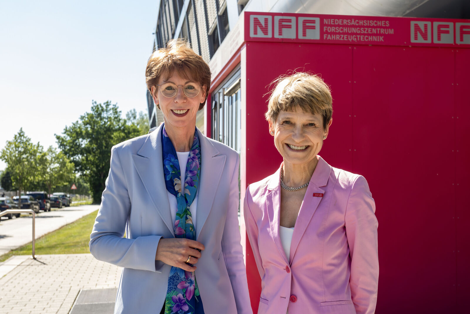 Zwei Frauen in Businesskleidung stehen lächelnd vor einem Gebäude mit NFF-Logo.